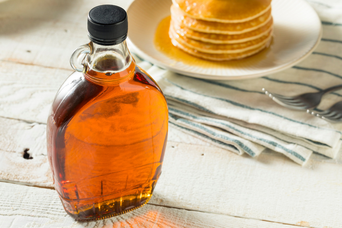 A bottle of maple syrup with stacked pancakes on a plate in the background