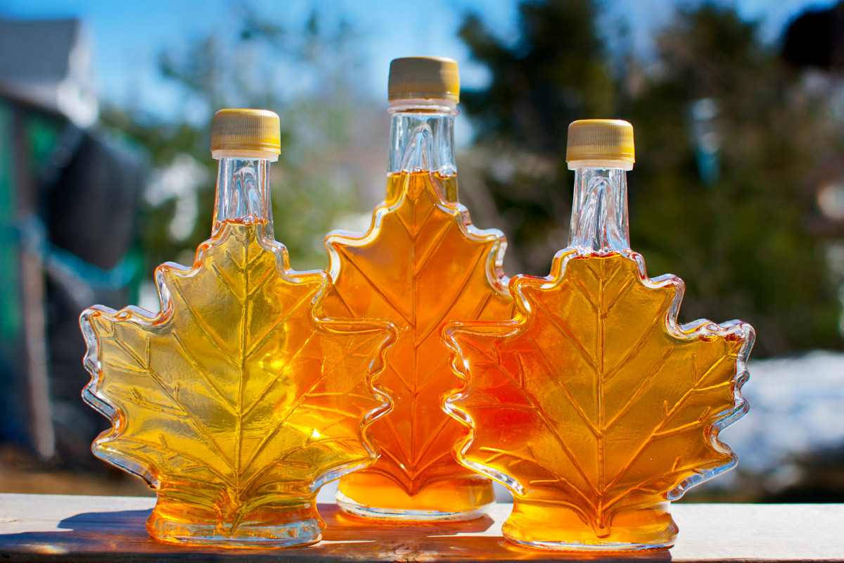 Three leaf-shaped bottles of maple syrup on a table outside