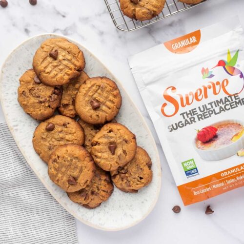 Low carb peanut butter cookies stacked on a oval white plate beside the package of sweetener