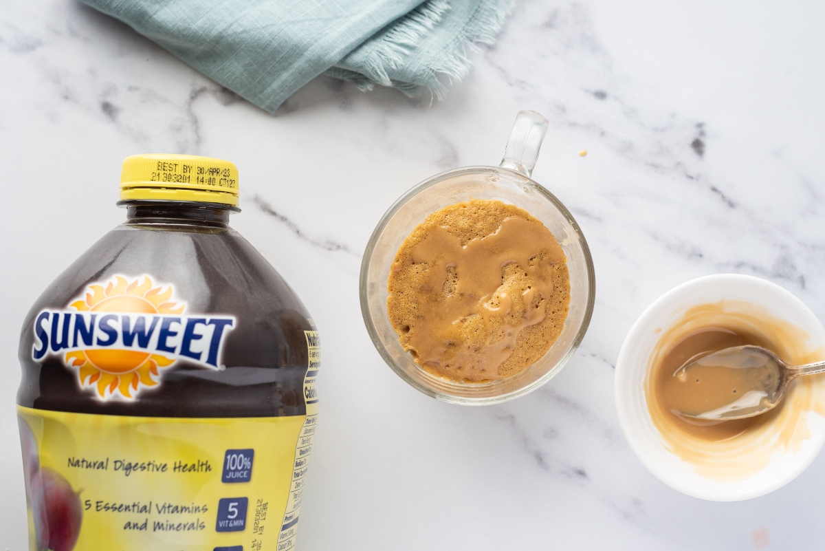 Blondie mug cake in a glass mug, batter for mug cake in a mug and a bottle of Sunsweet prune juice