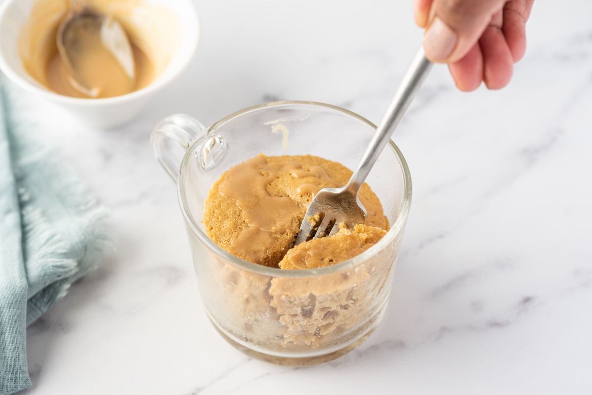 A person holding a fork in a mug cake in a glass mug