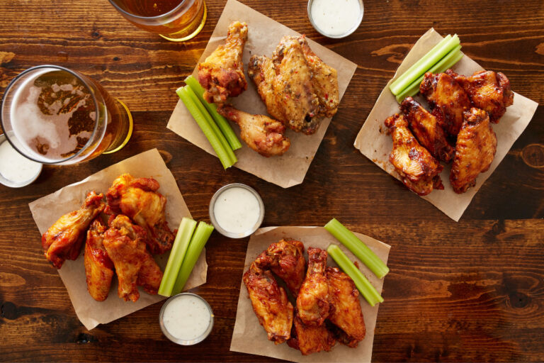 Buffalo chicken wings servings with vegetables and cups of sauce and two glasses of bear