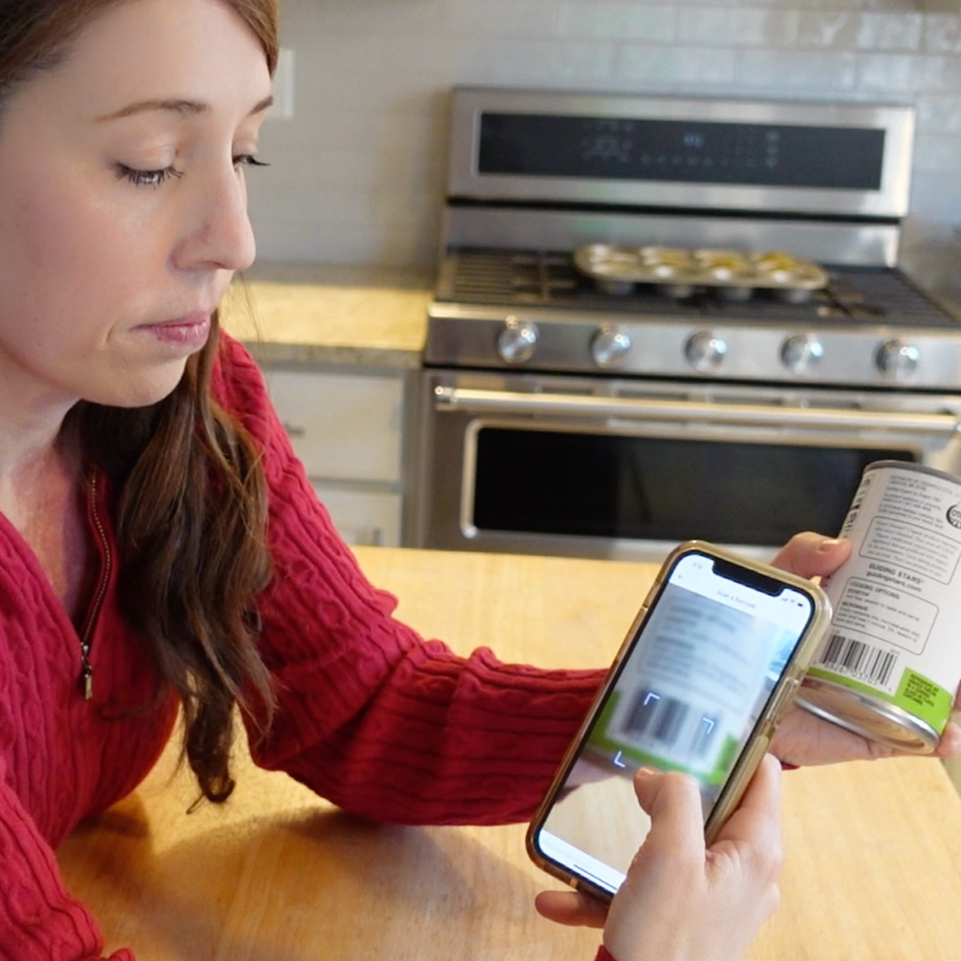 A woman holding a mobile with food app scanning a can's bar code
