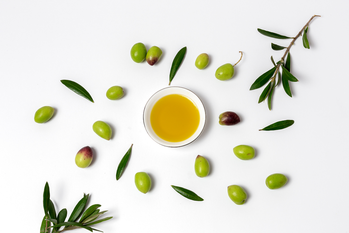 Olive oil in a white cup with scattered olives and olive branches around it