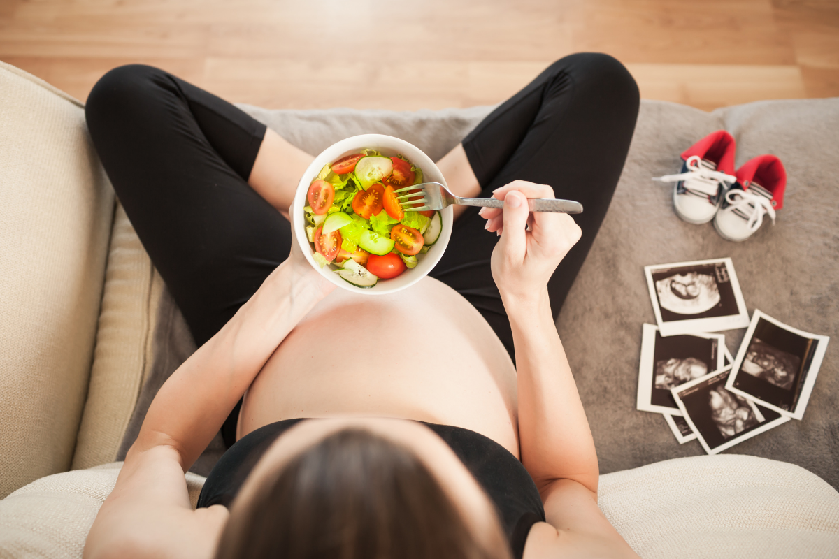 Pregnant woman eating a salad on a sofa