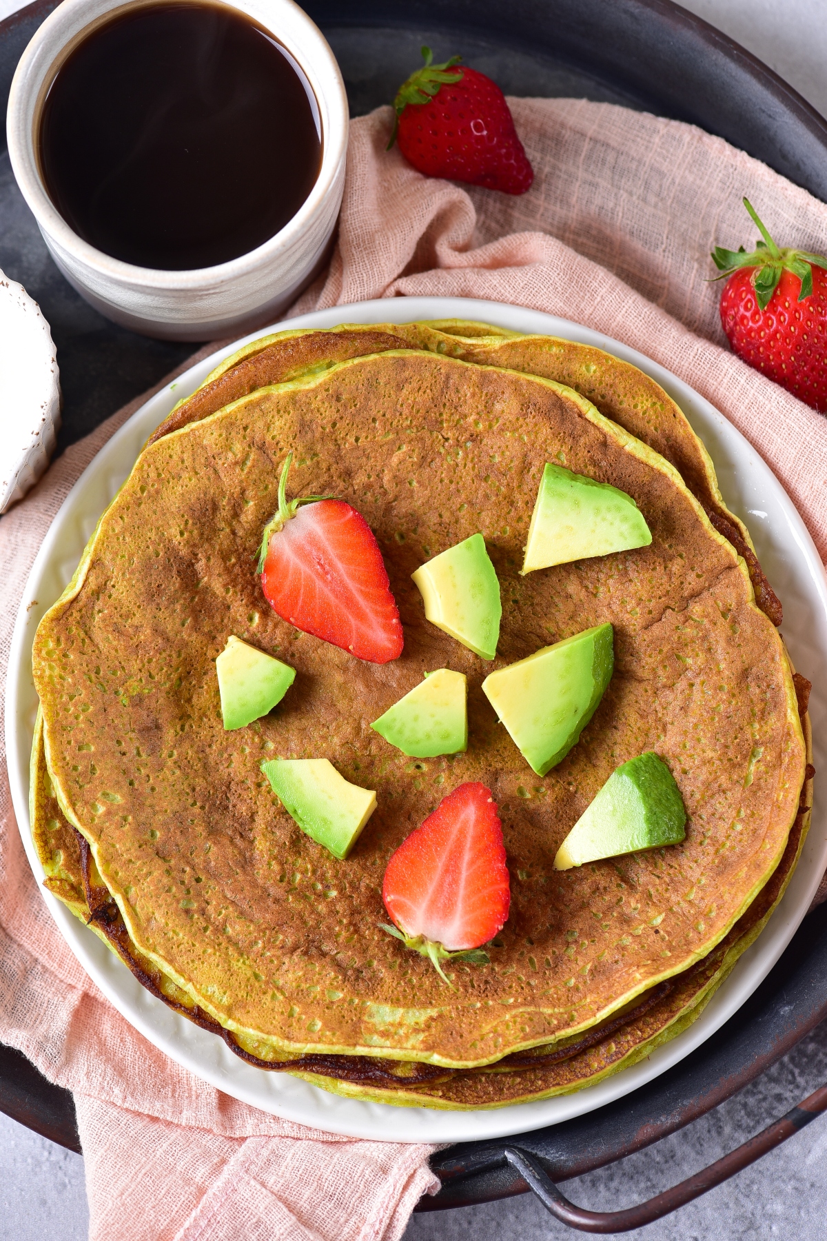 Avocado pancakes stacked on a plate topped with strawberries and chopped avocado