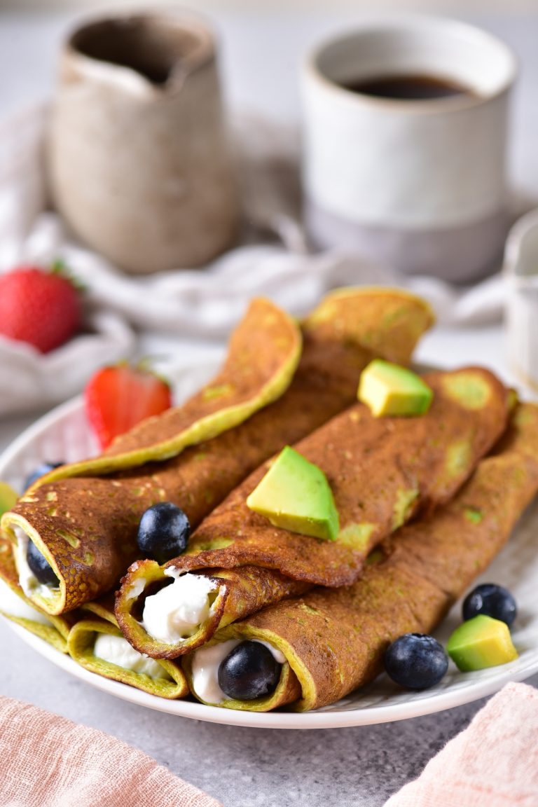 Roll up avocado pancakes served on a plate with chopped avocado, strawberries and blueberries on top