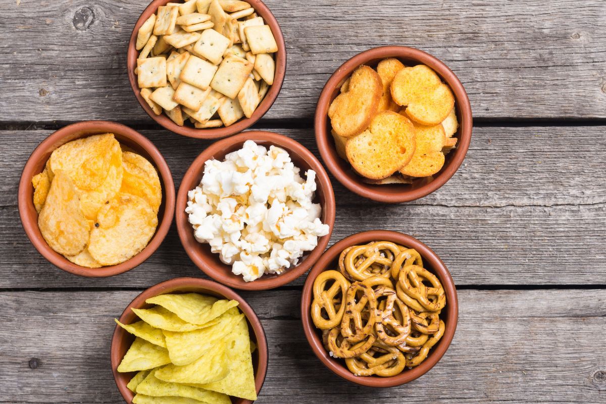 Bowls of crackers, chips, popcorn, pretzels on a wooden table