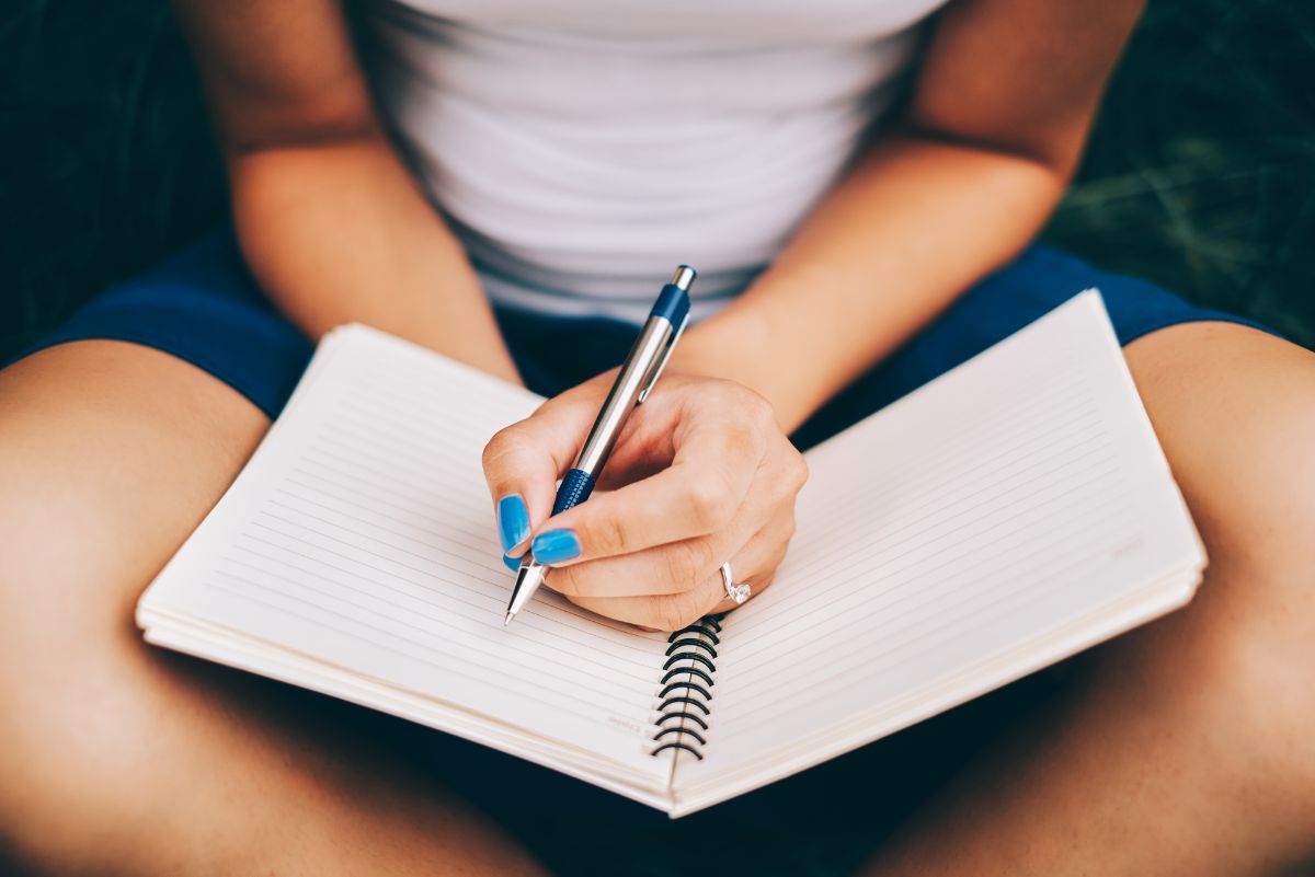 A woman sitting cross legged writing in a log book