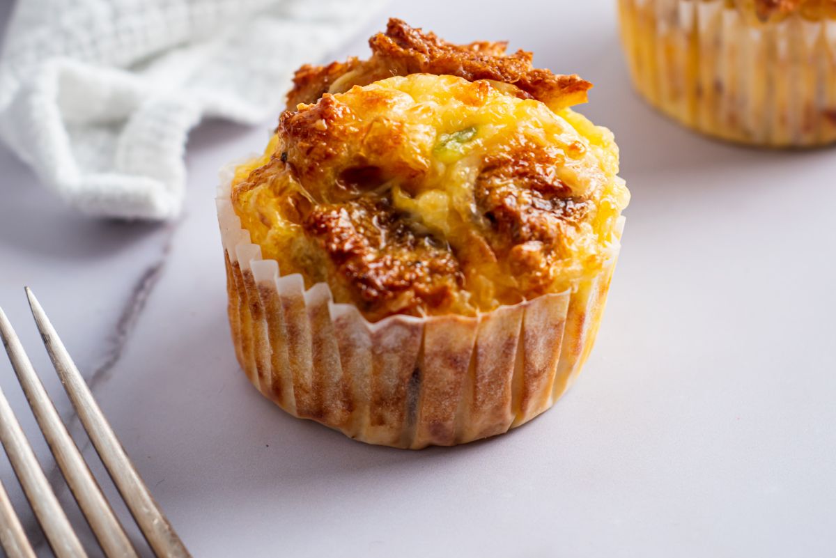 A baked veggie egg muffin with a white napkin in the background and a fork in front