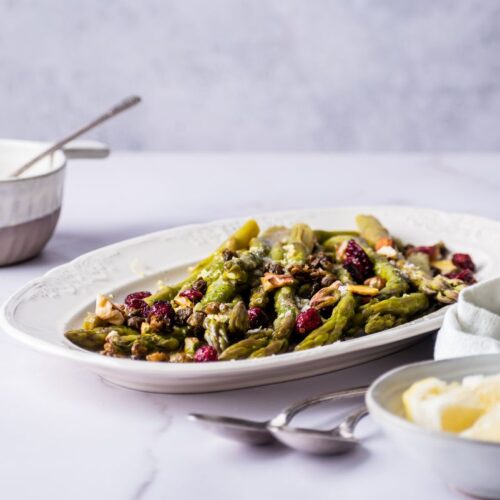 Instant pot asparagus on a plate garnished with berries next to a bowl of butter
