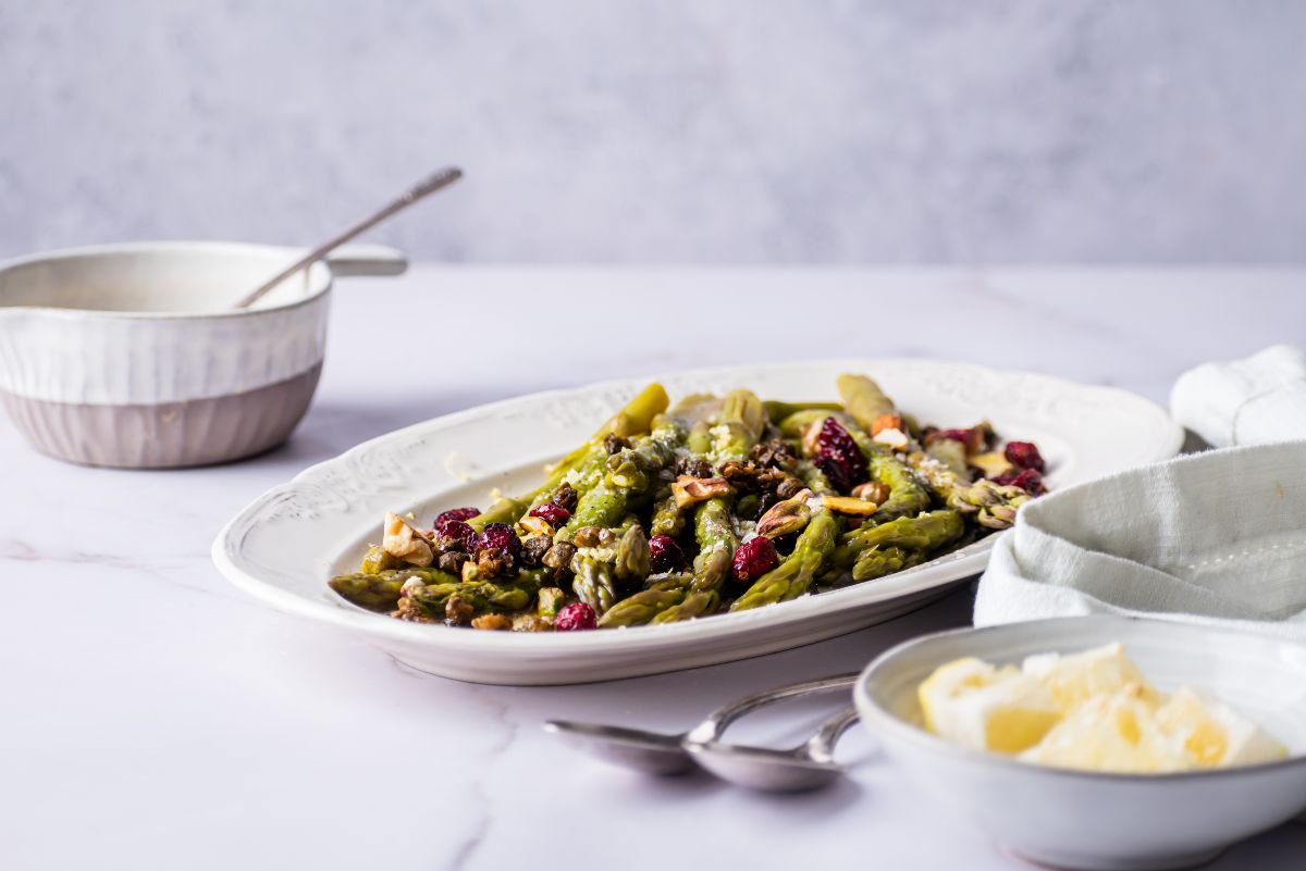 Instant pot asparagus on a plate garnished with berries next to a bowl of butter