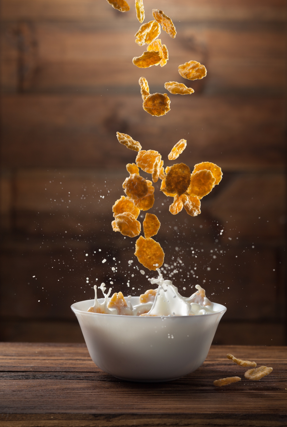 Falling corn flakes with milk splash on wooden background