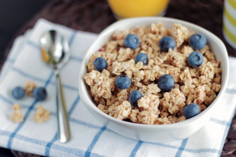 A bowl filled with whole grain cereals and blueberries with a spoon beside