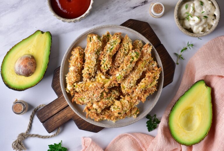 Crispy avocado bites with avocado cut in half on the side and a cup of ketchup