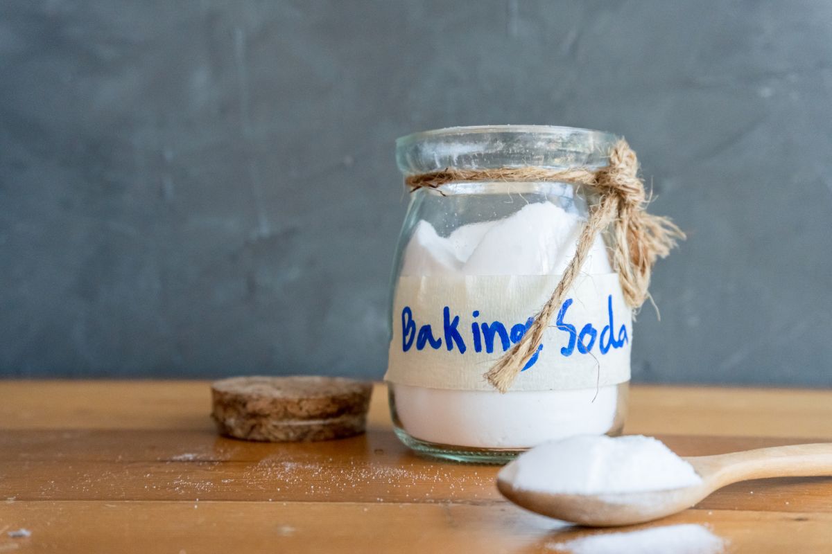 Baking soda in a jar and a spoon full of baking soda in front of the jar