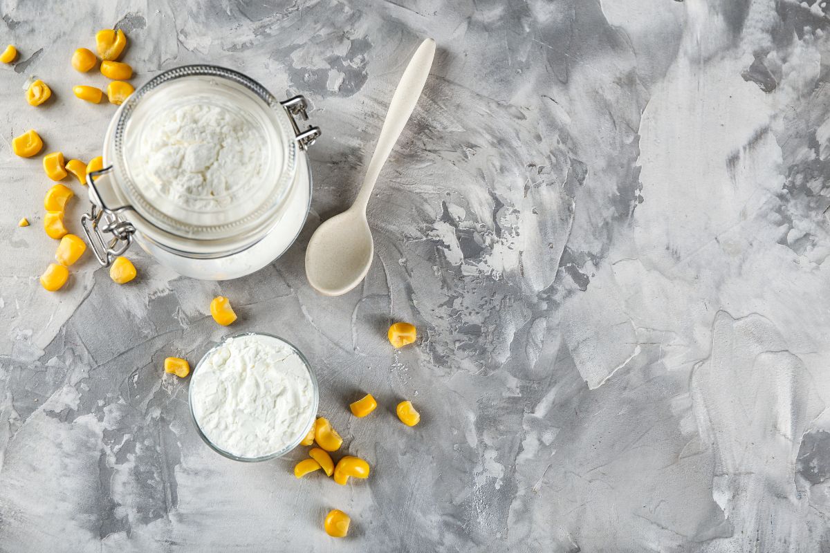 Cornstarch in a jar and kernels scattered around and a spoon