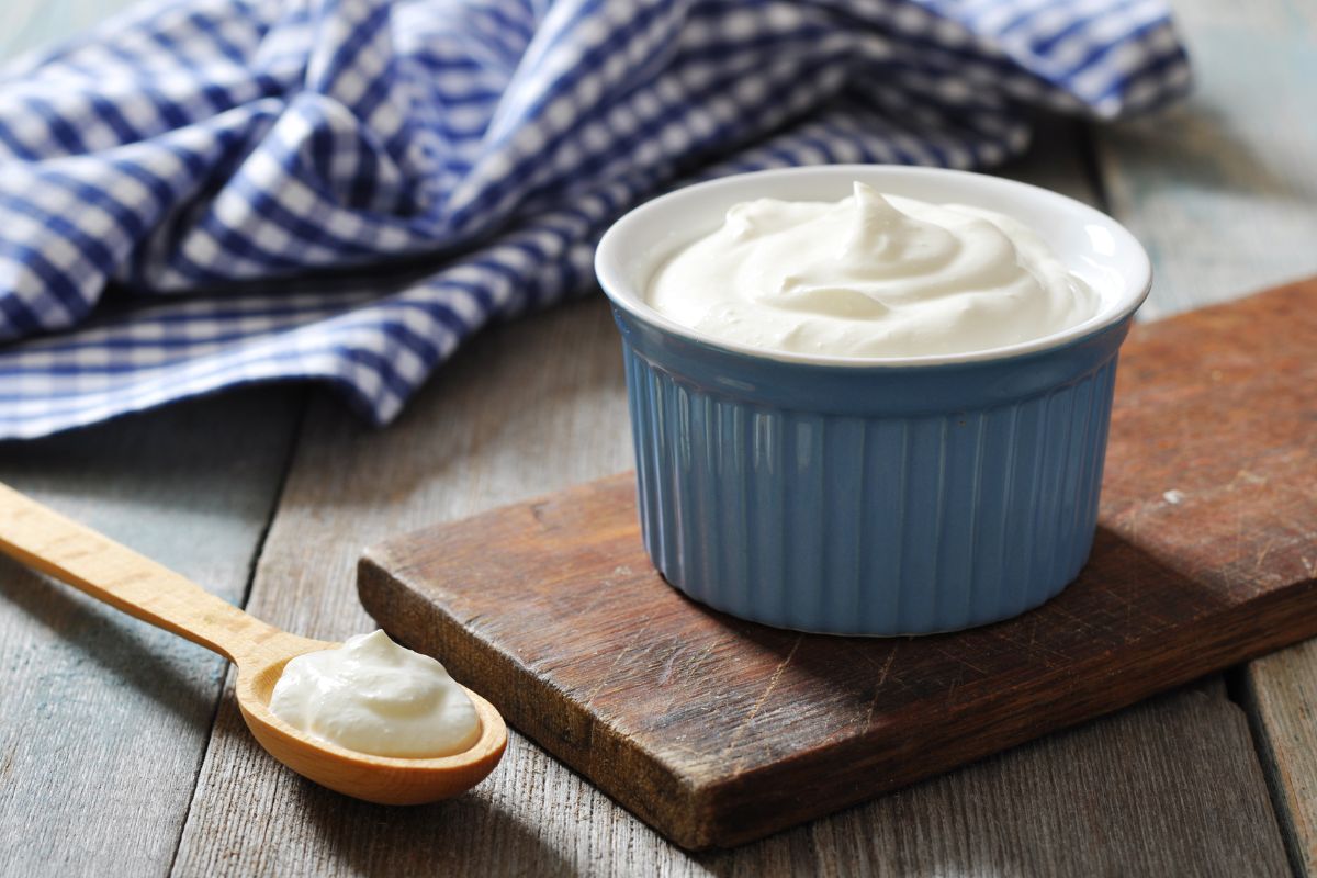 Greek yogurt in a cup on a wooden board and wooden spoon beside
