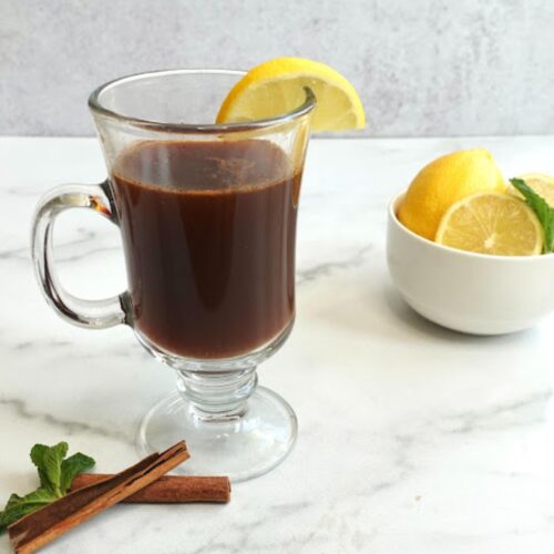 Prune juice hot toddy mocktail in a glass with cut lemon and cinnamon stick beside the glass