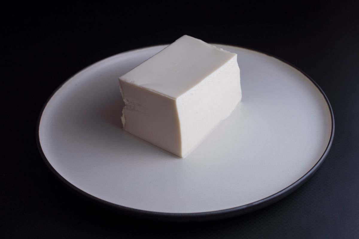 A piece of silken tofu on a white plate against the black background