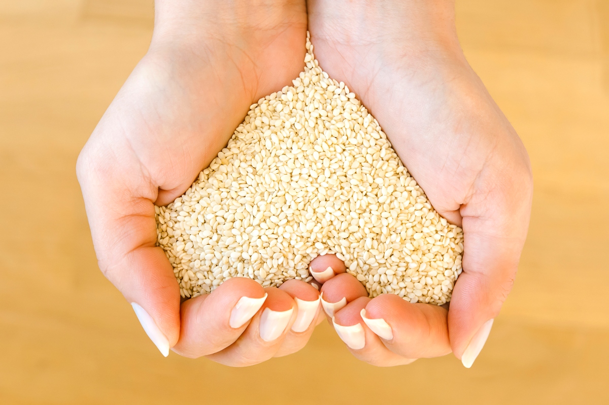 White sesame seeds in woman's hands forming heart shape