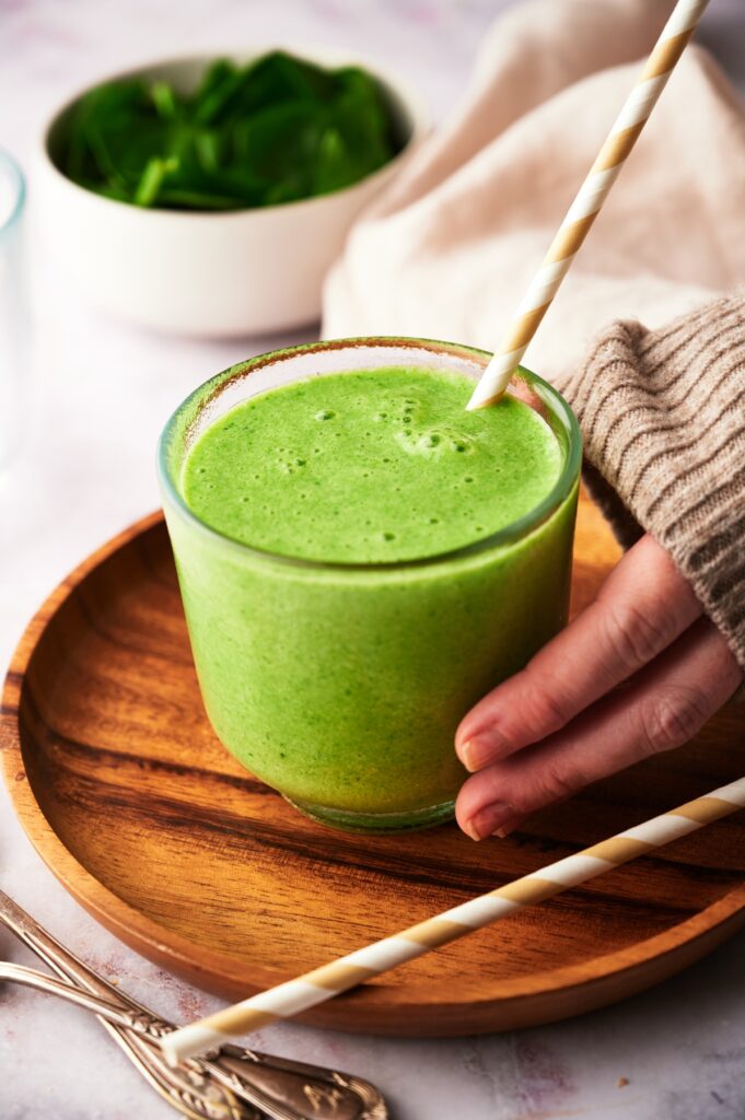 Person holding a glass with mango spinach smoothie