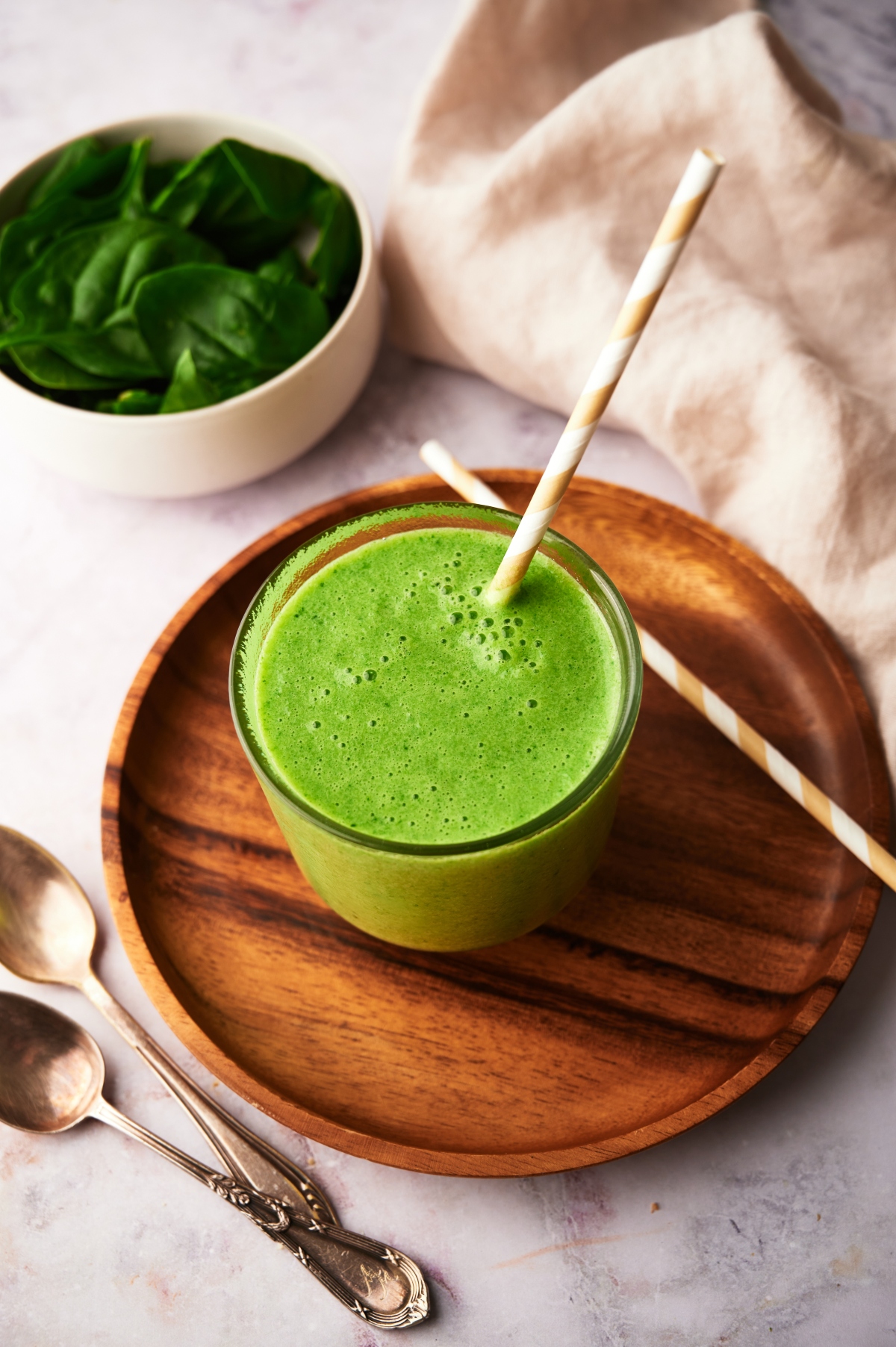Mango spinach smoothie in a glass on a wooden tray