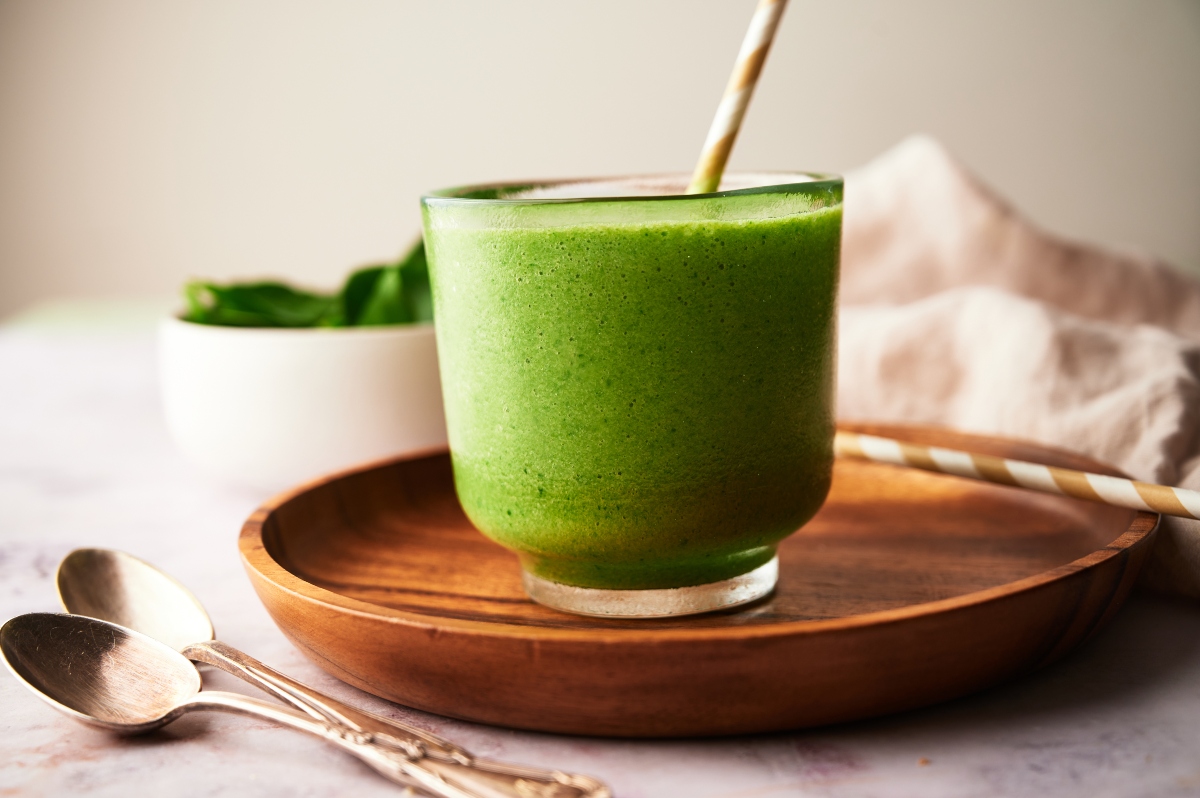 Mango spinach smoothie in a glass with a straw on a wooden tray