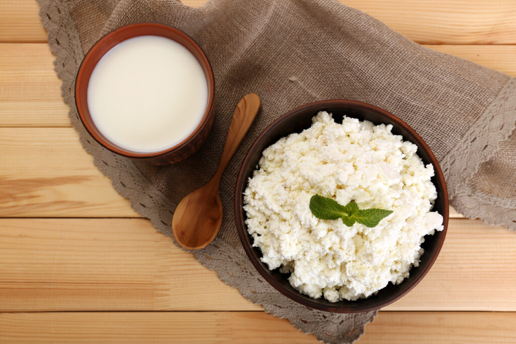 bowl of cottage cheese on a wooden board next to a bowl of milk