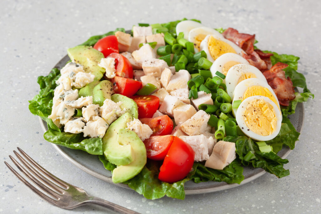 cobb salad on silver plate with fork on a white backrgound