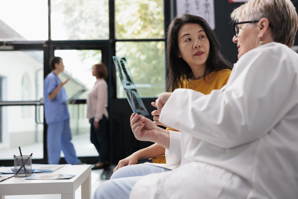 older woman doctor showing an x-ray to Asian woman to discuss results