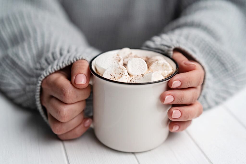 Woman holding cup with cacao and marshmallow while sitting at white table