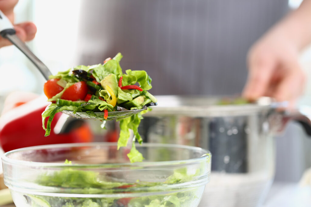clear salad bowl filled wit green salad with spoon lifting salad up to eat