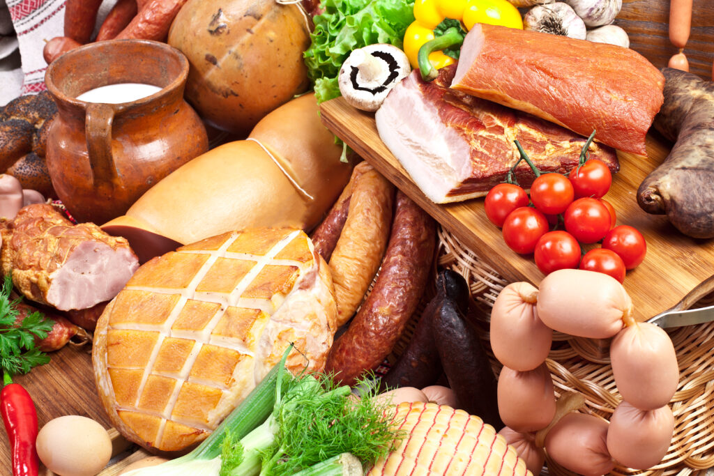 a variety of sausages on a tray with assorted produce to display foods to avoid with alpha gal syndrome