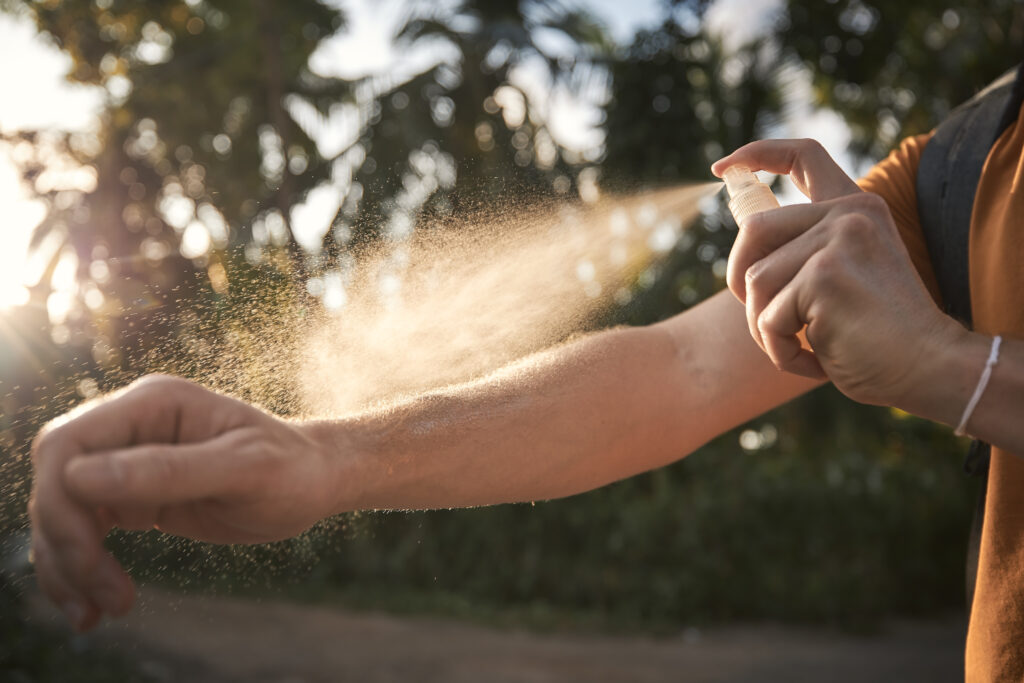 man spray insect repellant onto arm