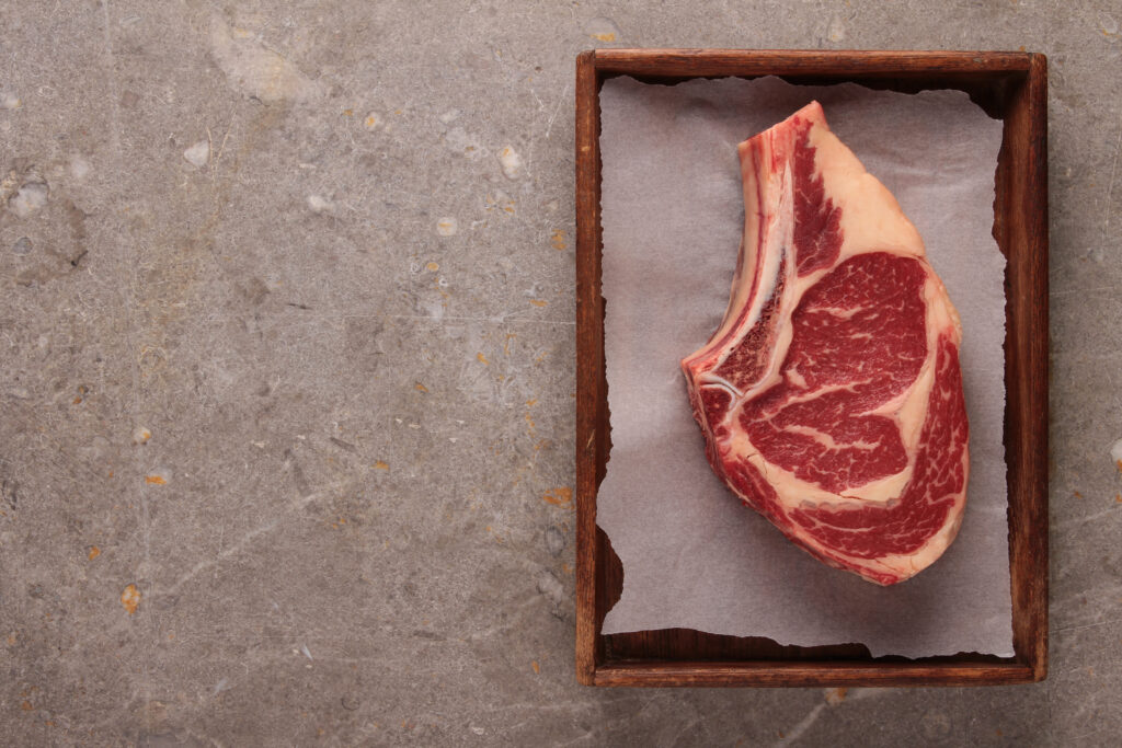 raw steak on wax paper on top of wooden cutting board on slate background to showcase what to avoid with a red meat allergy alpha gal diet