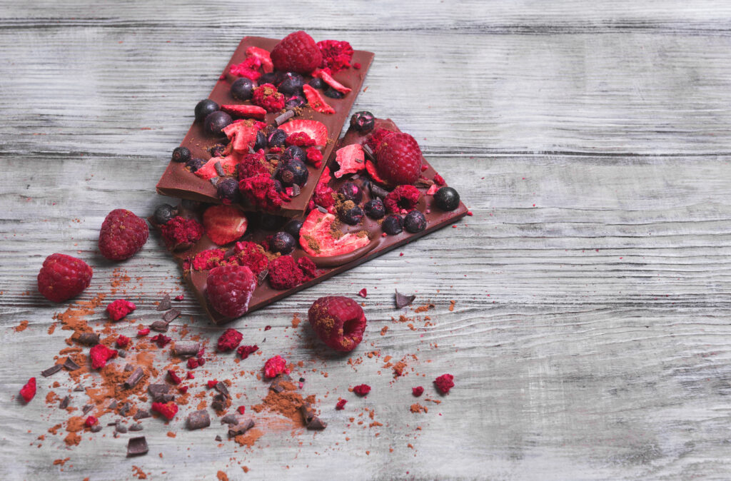 dark chocolate bar on light grey wooden background with freeze dried raspberries on top of dark chocolate to make a low carb chocolate bark