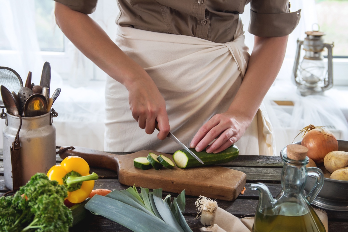Woman slice zucchini on wooden table near window. Rustic style.