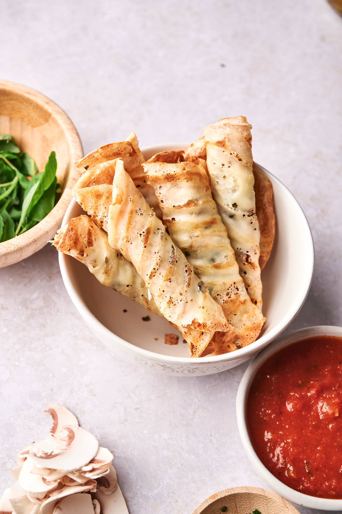 Keto Pizza Rolls in white bowl with marinara sauce and basil