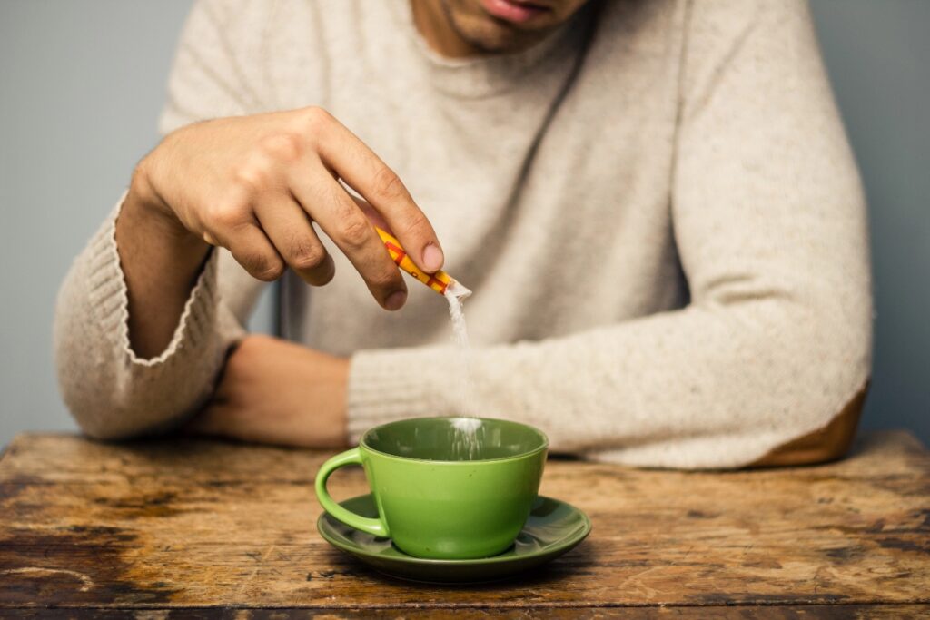 A person pouring sweetener into a green cup