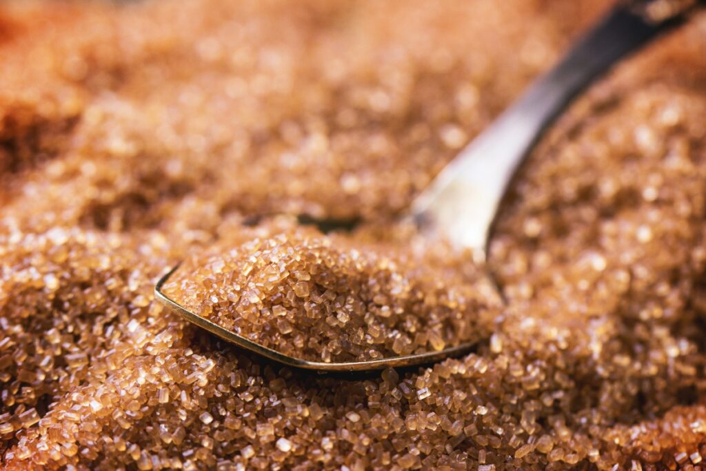 A pile of brown sugar and a spoon full of sugar on top of the pile