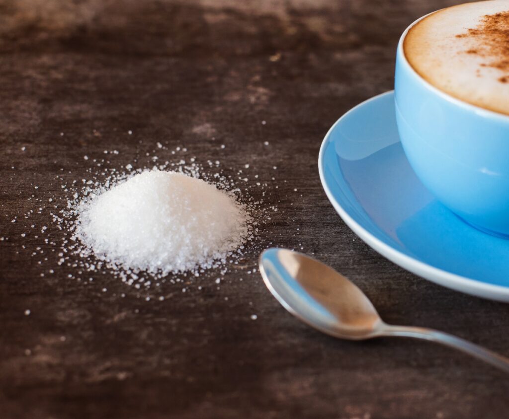 Blue coffee cup and a coffee spoon and scattered sweetener on a wooden surface