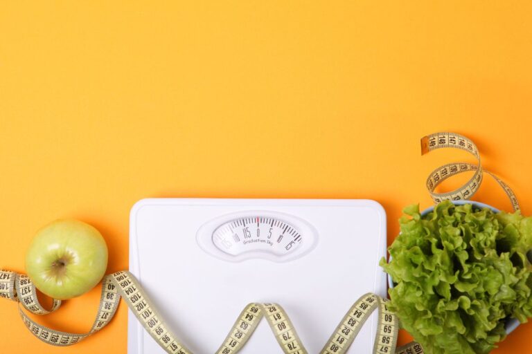Floor scale, measure tape, an apple and a salad against the yellow background