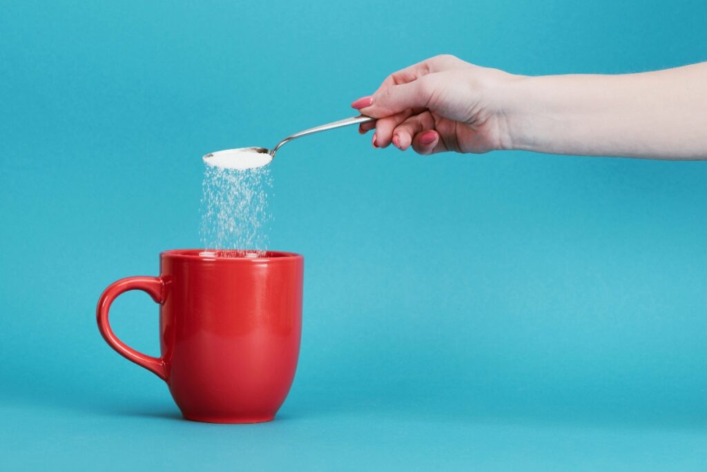 Woman pouring a sweetener from the spoon in a red mug against the blue background