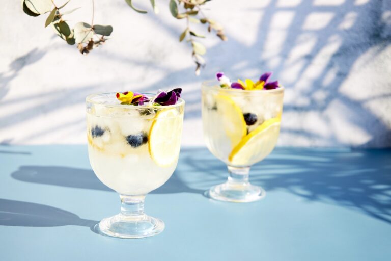 Iced soda with lemon and edible flowers under palm leaves on a bright sunny day