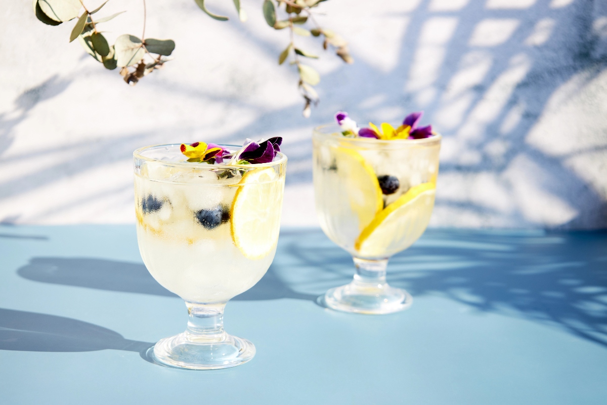 Iced soda with lemon and edible flowers under palm leaves on a bright sunny day