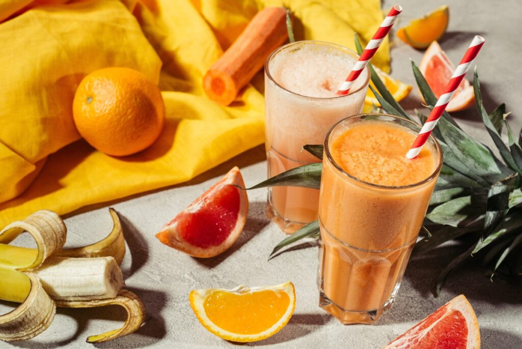 Glasses with tropical fruits juice and fruit pieces on grey table